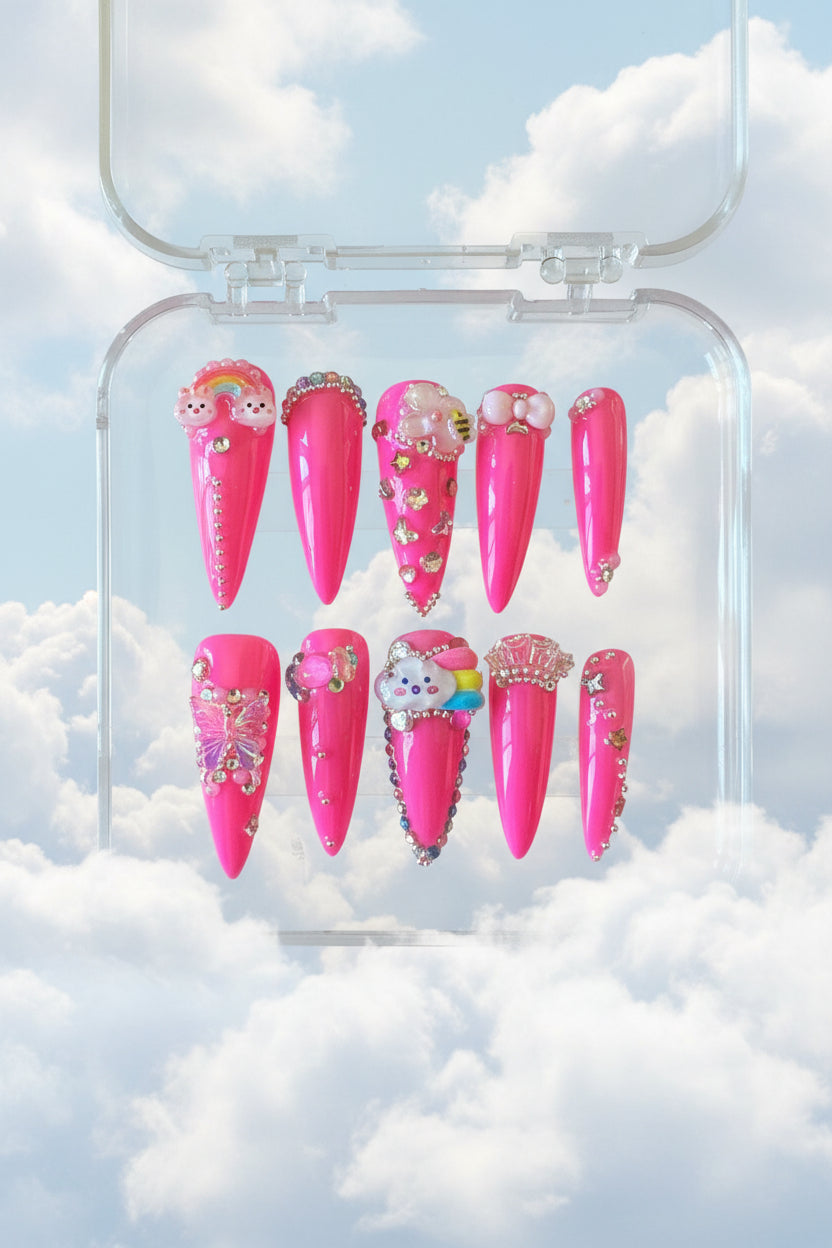 Pink nail art designs with decorations in a clear plastic case on a wooden surface